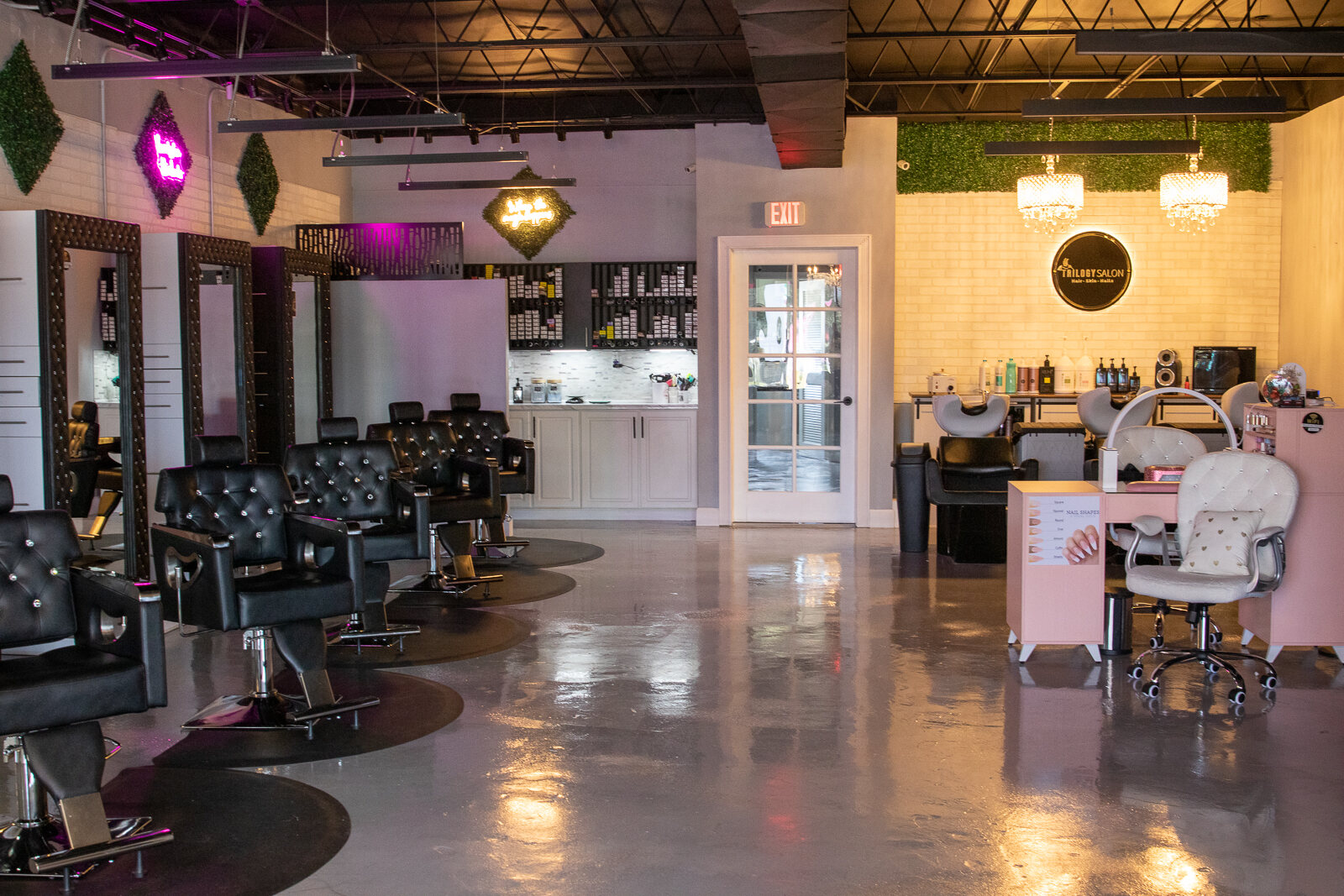 Inside Trilogy Salon: black tufted styling chairs, framed mirrors, chandeliers and the round Trilogy Salon sign