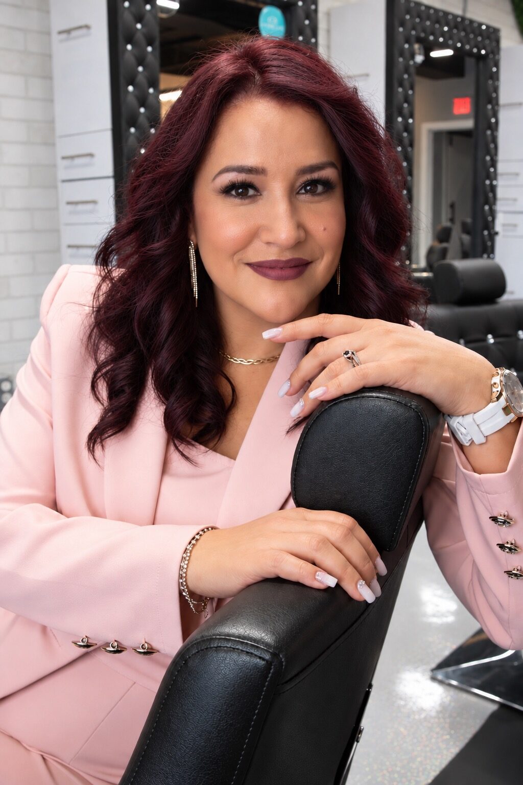 Mara Venegas, owner of Trilogy Salon, leaning on a styling chair inside the salon
