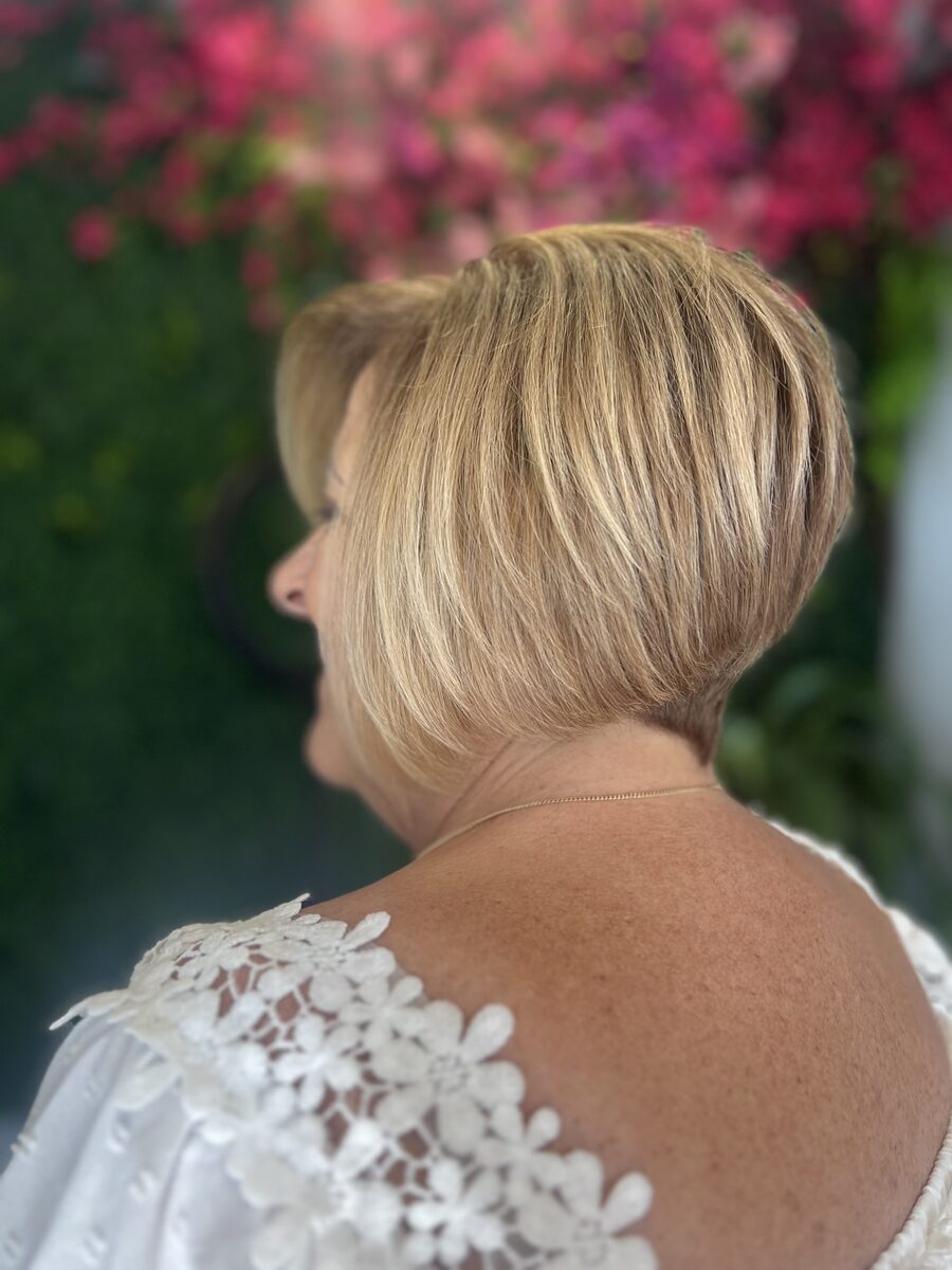A short stacked blonde bob seen from the side in front of the flower wall