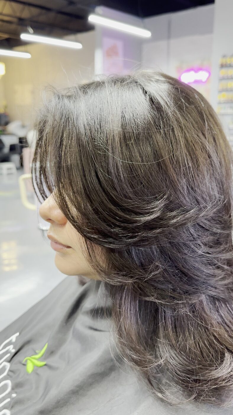 Dark layered cut with curtain bangs, seen from the side