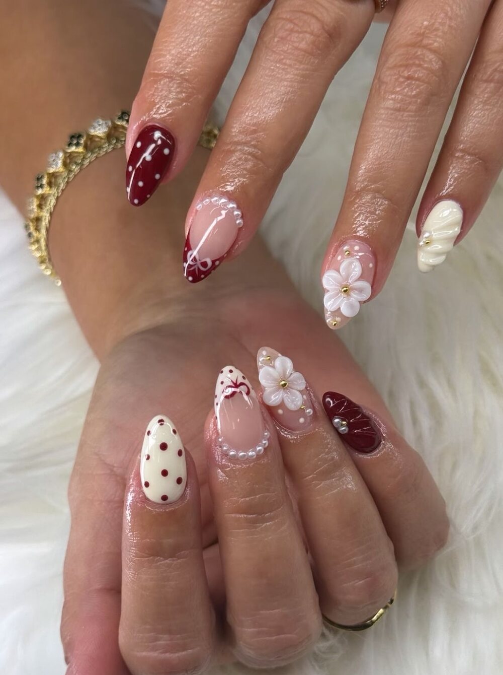 Almond nails in burgundy and cream with pearls, white sculpted flowers and bows