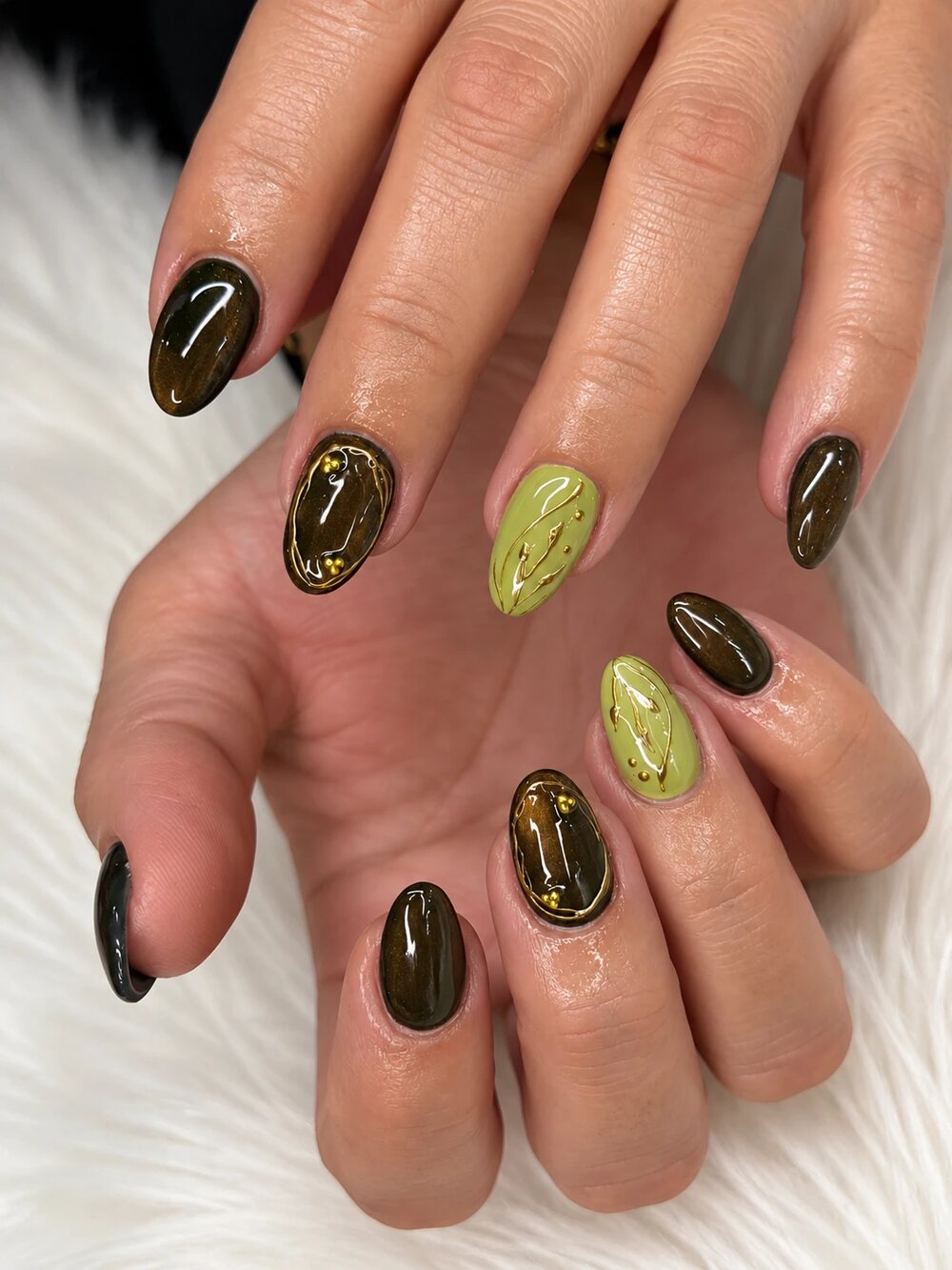 Short almond nails in a dark cat-eye brown and olive green with gold line art